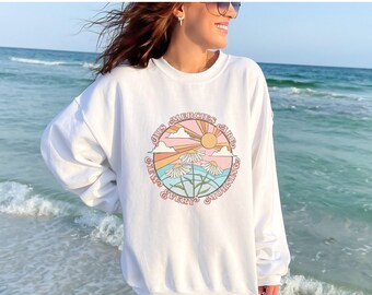 May include: White sweatshirt with a graphic print of a sun, clouds, and daisies in a circle. The text around the graphic says "Just Emerges, Jared, New Every Morning".