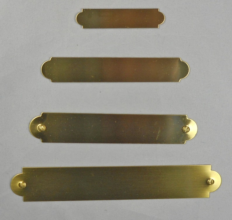 Puede incluir: Cuatro placas de nombre de lat&oacute;n con bordes redondeados y agujeros para tornillos. Las placas de nombre est&aacute;n dispuestas en una pila vertical, con la m&aacute;s peque&ntilde;a en la parte superior y la m&aacute;s grande en la parte inferior.
