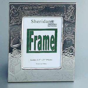 May include: Silver-toned photo frame with an embossed design. The frame has a green inscription that reads "Frame" and holds a 3.5" x 5" photo. The frame is made in China.
