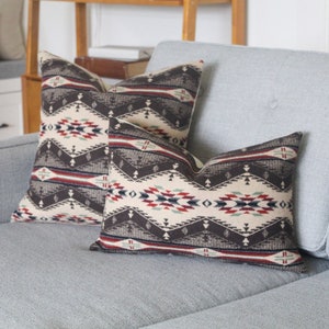 May include: Two throw pillows with a geometric pattern in shades of brown, red, white, and blue. The pillows are on a light grey sofa.