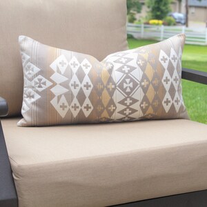 May include: A brown outdoor chair with a beige cushion and a patterned throw pillow. The pillow has a geometric design with white, brown, and gold accents.