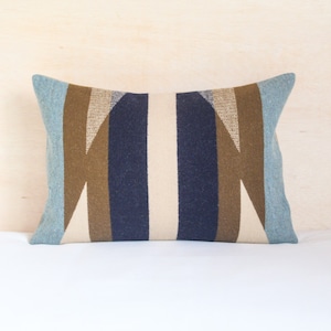 May include: A decorative pillow with a geometric pattern in shades of blue, brown, and beige. The pillow has a rectangular shape and is made of a soft, textured fabric.