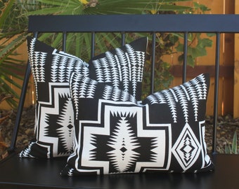 May include: Two black and white patterned throw pillows on a black metal bench. The pillows have a geometric design with black and white triangles and diamonds.
