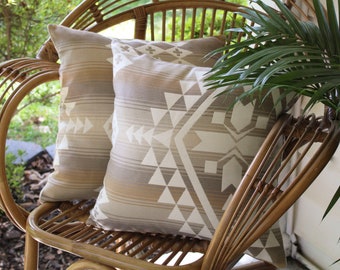 May include: Two patterned throw pillows on a wicker chair with a green plant in the background.