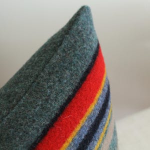 May include: A close-up of a green, red, blue, yellow, and beige striped pillow. The pillow is made of a soft, fuzzy material.