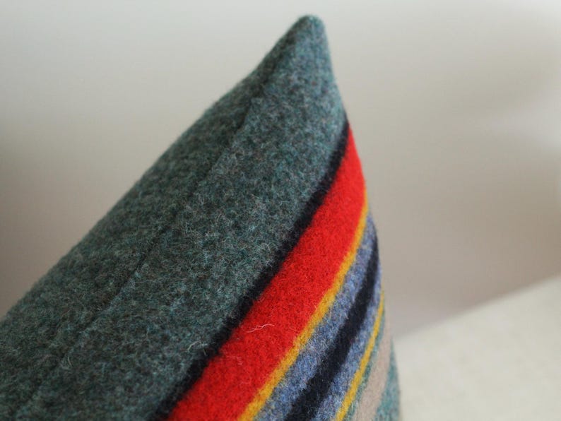 May include: A close-up of a green, red, blue, yellow, and beige striped pillow. The pillow is made of a soft, fuzzy material.