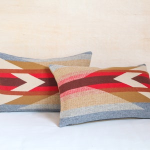 May include: Two decorative throw pillows with a geometric pattern in shades of brown, red, white, and blue. The pillows are made of a woven fabric and have a subtle texture.