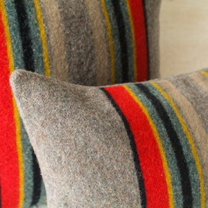 May include: Two striped throw pillows with a brown, red, yellow, blue and black pattern. The pillows are made of a soft, fuzzy material.