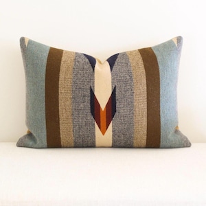 May include: Rectangular cushion with a woven, striped pattern in shades of blue, brown, and beige. The cushion features a central geometric design in cream, brown, and orange tones, adding a Southwestern or tribal aesthetic.