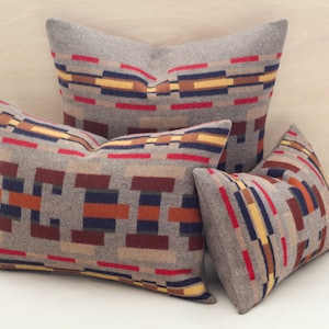 May include: Three decorative throw pillows featuring a geometric pattern in shades of grey, red, brown, blue, and yellow. The pillows are made from a soft, textured fabric.