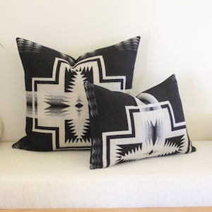 May include: Two decorative throw pillows with a geometric pattern. The pillows are black with a white and gray design. The pillows are rectangular and are placed on a white bench.