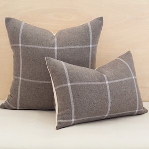 May include: Two brown and white plaid throw pillows with a white background. The larger pillow is behind the smaller pillow.