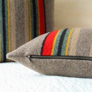 May include: Two striped throw pillows with a zipper closure. The pillows are made of a brown, grey, red, black and yellow striped fabric.