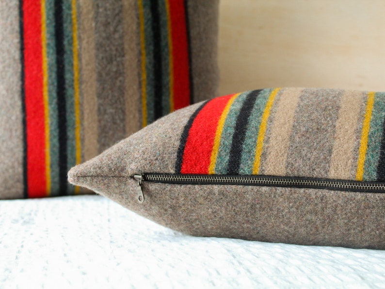 May include: Two striped throw pillows with a zipper closure. The pillows are made of a brown, grey, red, black and yellow striped fabric.