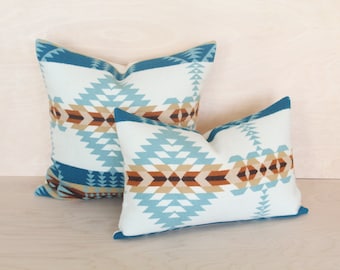May include: Two decorative throw pillows with a geometric pattern in shades of blue, brown, and white. The larger pillow has a teal blue border and the smaller pillow has a light blue border.