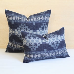 May include: Two decorative throw pillows with a geometric pattern in shades of blue and white. The larger pillow is behind the smaller pillow.