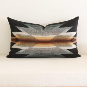 Peut inclure: Coussin rectangulaire décoratif avec un fond noir et un motif géométrique dans les tons de gris, vert, marron et jaune. Le coussin est posé sur une surface blanche, mettant en valeur son design et ses couleurs.