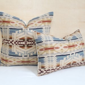 May include: Two decorative throw pillows with a geometric pattern in shades of blue, brown, beige, and red. The pillows are made of a soft, woven fabric.