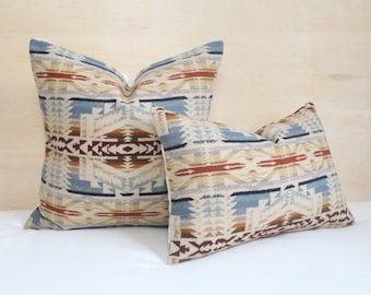 May include: Two decorative throw pillows featuring a geometric pattern in shades of blue, brown, beige, and red. The pillows are made from a soft, woven fabric.