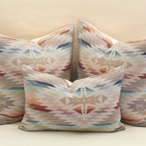 May include: Three decorative throw pillows featuring a geometric pattern in shades of brown, beige, blue, and red. The pillows are arranged in a triangular formation.