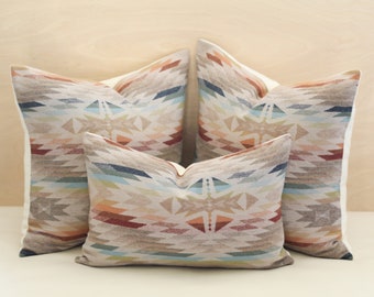 May include: Three decorative throw pillows featuring a geometric pattern in shades of brown, beige, blue, and red. The pillows are arranged in a triangular formation.