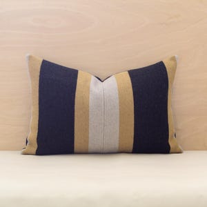 May include: A striped throw pillow with black, white and gold stripes. The pillow is made of a soft, textured fabric.