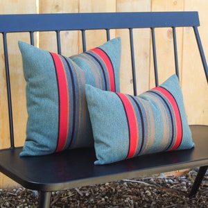 May include: Two striped throw pillows on a black metal bench. The pillows are teal with red, black, and brown stripes.