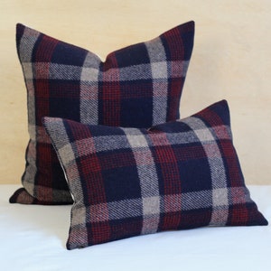 May include: Two plaid cushion covers, one larger than the other, with a navy blue, red and beige plaid pattern. The cushions are on a white bedspread.