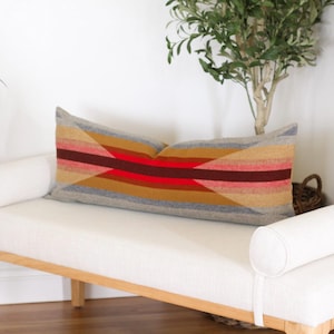 May include: A white bench with a wooden frame and a long, rectangular pillow with a geometric pattern in shades of red, orange, brown, and gray.