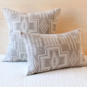 May include: Two decorative throw pillows with a geometric pattern in shades of gray and white. The pillows are made of a soft, textured fabric and feature a repeating design of triangles and diamonds.