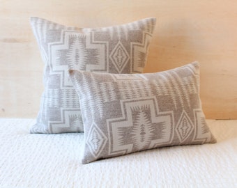 May include: Two decorative throw pillows with a geometric pattern in shades of gray and white. The pillows are made of a soft, textured fabric and feature a repeating design of triangles and diamonds.