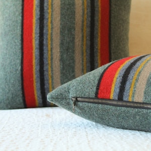 May include: Two green striped throw pillows with red, yellow, and black stripes. The pillow on the right has a zipper closure.
