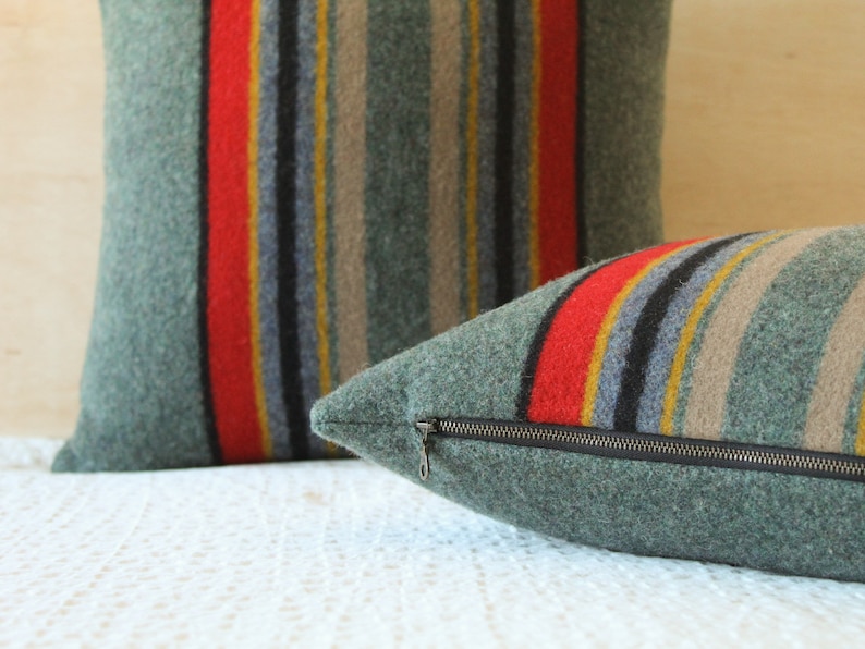 May include: Two green striped throw pillows with red, yellow, and black stripes. The pillow on the right has a zipper closure.