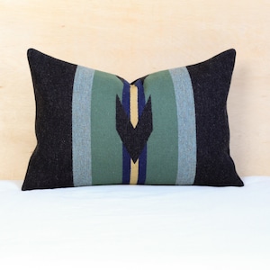 May include: A rectangular cushion with a black background and a central design of vertical stripes in green, blue, and yellow. The cushion has a geometric pattern in the centre.