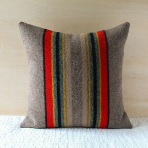 May include: A grey throw pillow with red, yellow and blue stripes. The pillow is made of a soft, textured fabric.