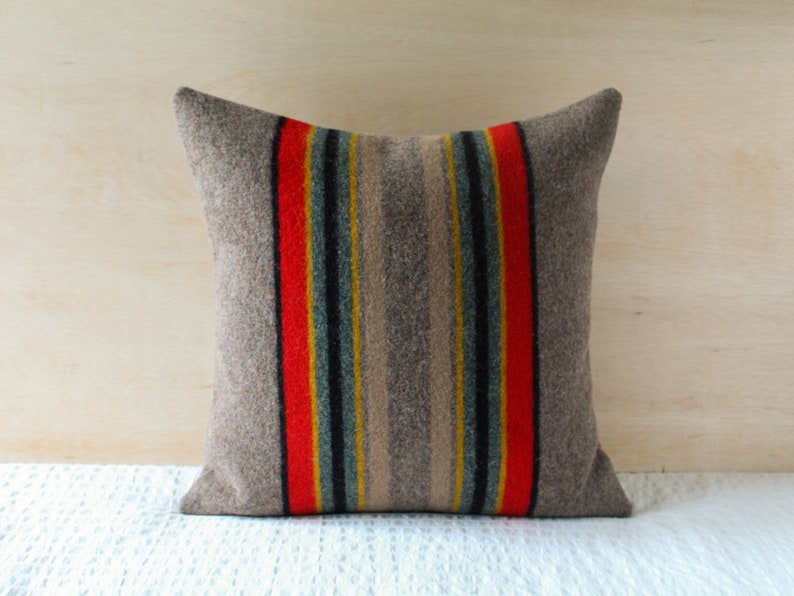 May include: A grey throw pillow with red, yellow and blue stripes. The pillow is made of a soft, textured fabric.