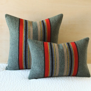 May include: Two decorative pillows with a striped pattern in shades of green, red, yellow, and black. The pillows are made of a soft, textured fabric.