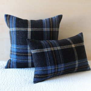 May include: Two plaid throw pillows in shades of blue, black, and tan. The larger pillow is behind the smaller pillow.