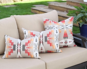 May include: Four patterned throw pillows with geometric designs in shades of red, orange, gray, and white on a beige couch.