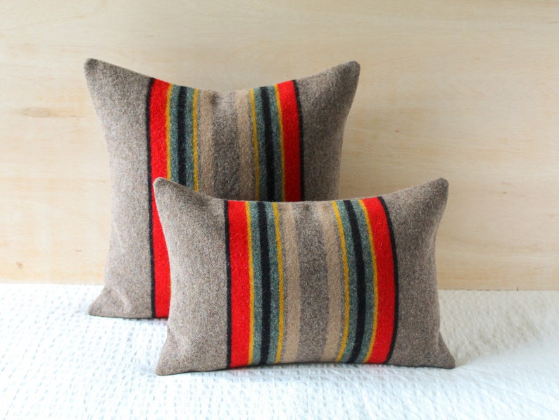 May include: Two decorative throw pillows with a striped pattern in shades of grey, red, yellow, blue, and black. The pillows are made of a soft, textured fabric.