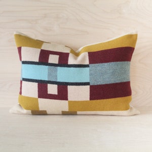 May include: A rectangular cushion with a geometric pattern in shades of mustard yellow, burgundy, cream, and light blue.