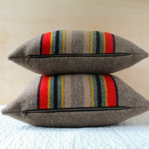 May include: Two brown wool throw pillows with a zipper closure. The pillows have a striped pattern in red, yellow, blue, and grey.