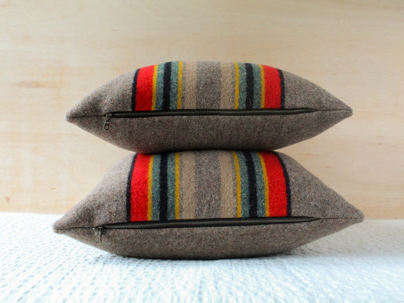 May include: Two brown wool throw pillows with a zipper closure. The pillows have a striped pattern in red, yellow, blue, and grey.