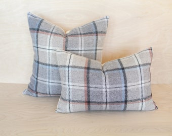 May include: Two decorative throw pillows with a plaid pattern in shades of grey, white, and light blue. The larger pillow is behind the smaller pillow.