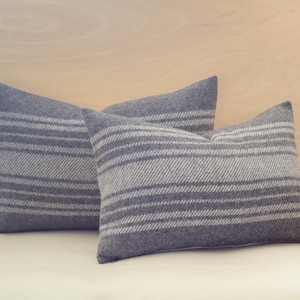 May include: Two grey and white striped throw pillows with a subtle herringbone pattern. The pillows are arranged on a white surface.