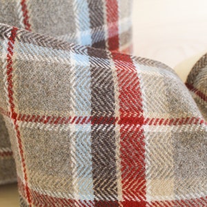 Op de afbeelding: Twee kussens met een rood, bruin, beige en blauw geruit patroon.