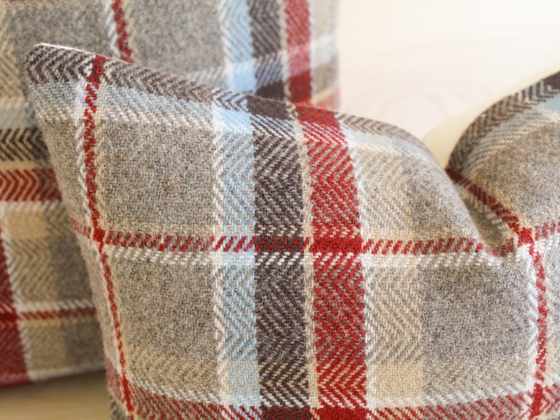 Op de afbeelding: Twee kussens met een rood, bruin, beige en blauw geruit patroon.