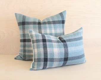 May include: Two decorative throw pillows with a blue and white plaid pattern. The larger pillow is behind the smaller pillow.