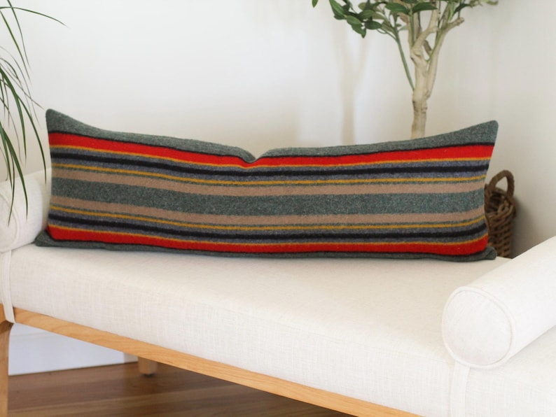 May include: A long, rectangular pillow with a striped pattern in shades of gray, red, yellow, and black. The pillow is made of a soft, woven fabric and is perfect for adding a touch of color and texture to any room.