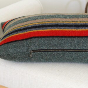 May include: A striped throw pillow with a zipper closure. The pillow is made of a soft, fuzzy fabric and has a green, red, yellow, and blue color scheme.
